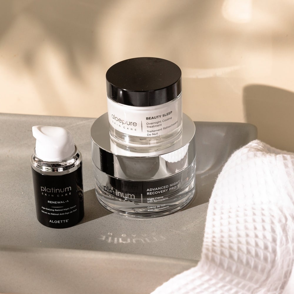 Aloette Platinum Renewal-A serum, Advanced Night Recovery Pro and Aloepure Beauty Sleep jars on a grey stone tray beside a white waffle towel