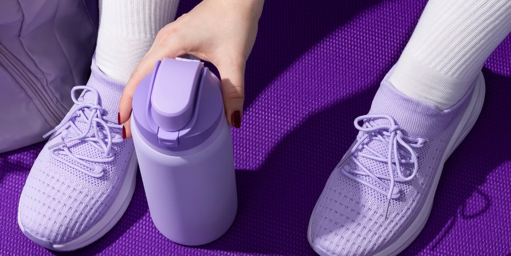 Woman in lavender sneakers on a purple yoga mat reaching for a lavender water bottle