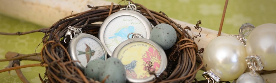 Silver locket charms with bird prints and pearl charms resting in a small twig nest