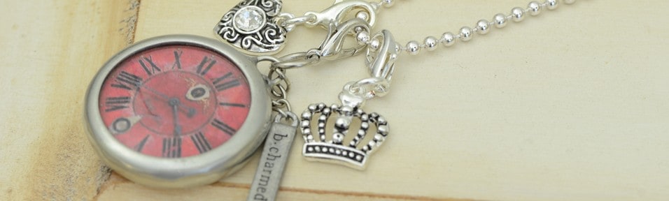 A red-faced pocket-watch locket and a silver crown charm hanging from a chain on cream paper