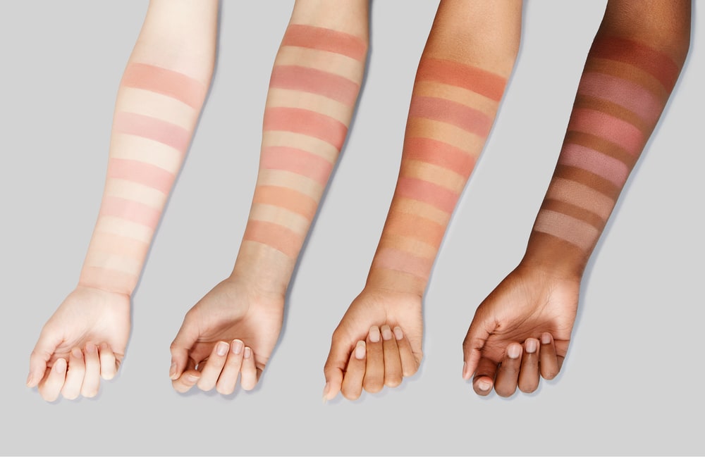 Four forearms with different skin tones, each swatched with six shades of BeCause Illuminating Blush