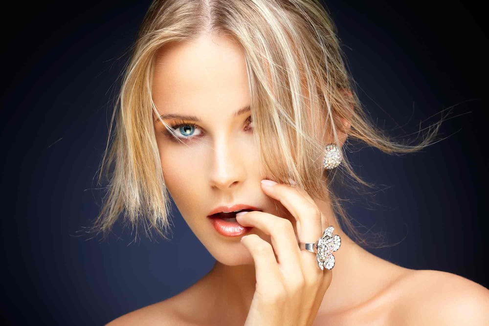 A blonde woman wearing a sparkling crystal stud earring and a large crystal flower cocktail ring