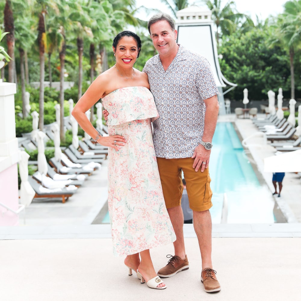 Bellame co-founders Melissa and Scott Thompson standing by a resort pool lined with palm trees