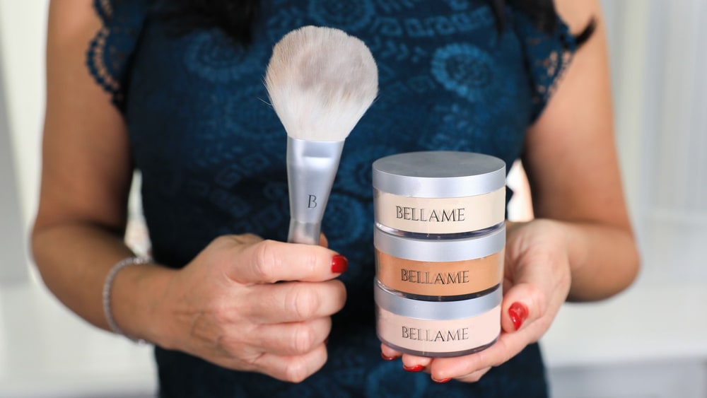 A woman holding a Bellame powder brush and a stack of three loose powder jars