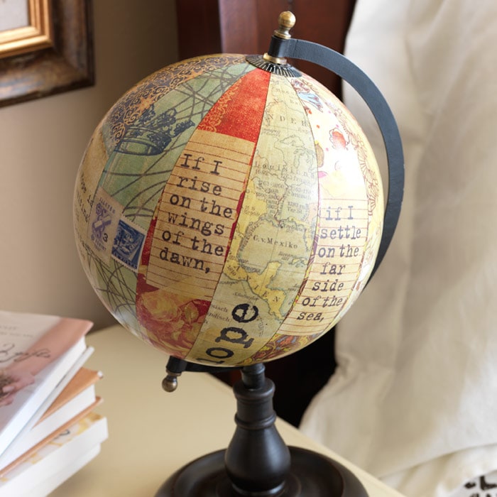 A decoupage globe printed with a Psalm verse on a dark stand, beside a stack of books on a desk