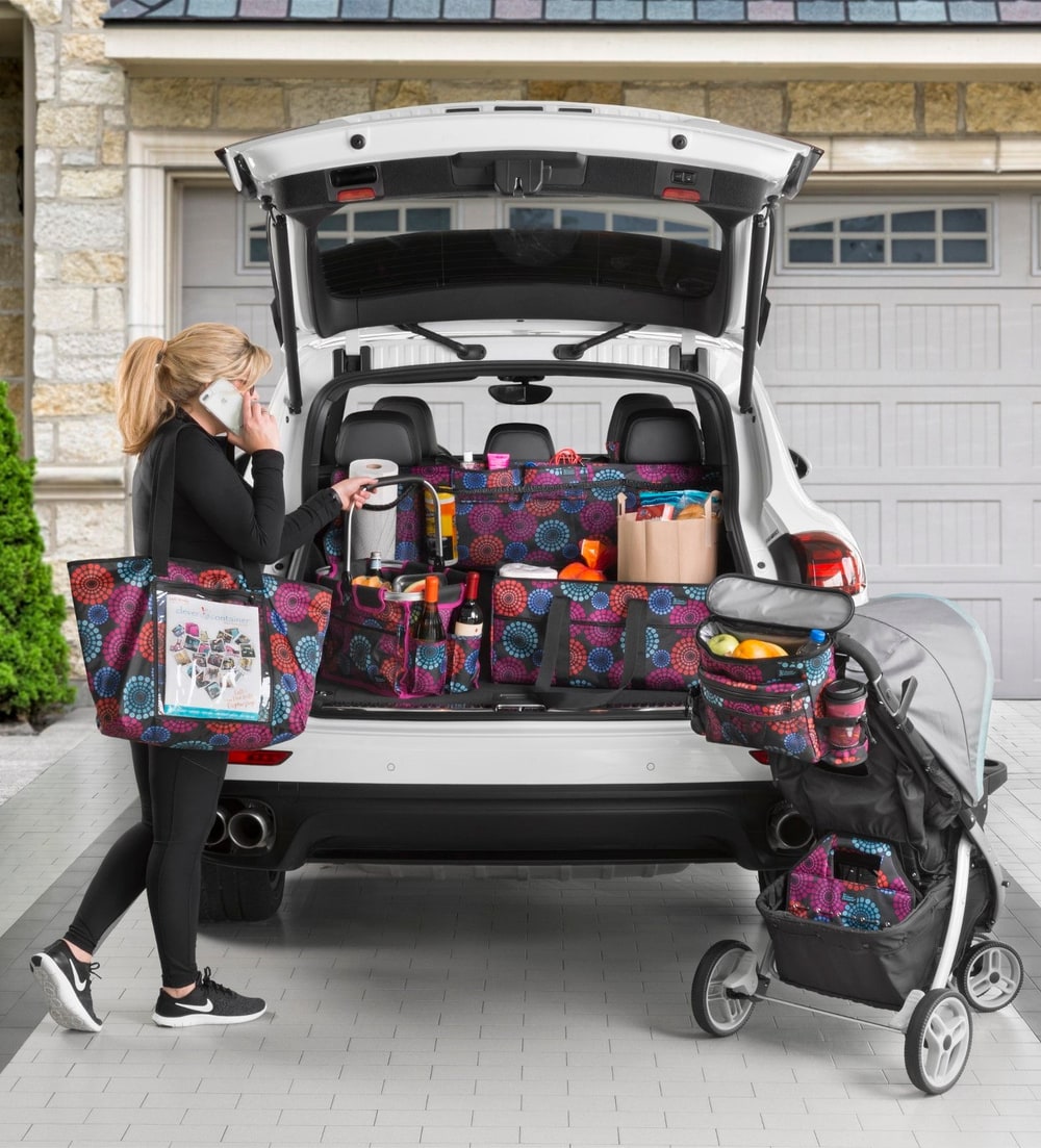 A woman loading patterned Clever Container totes and trunk organizers into the back of an SUV beside a stroller