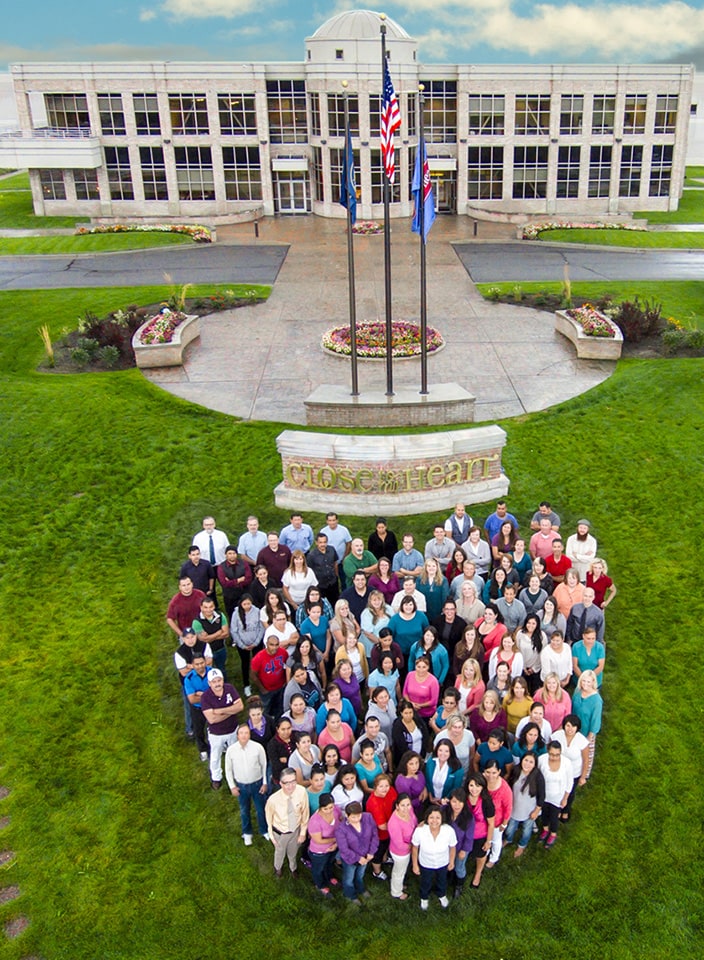 Close To My Heart home office staff standing on a lawn in the shape of a heart in front of the company's office building