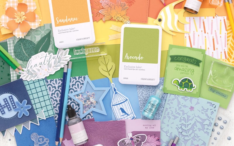 A rainbow flat lay of Close To My Heart ink pads, clear stamps, cardstock, embellishments and handmade cards