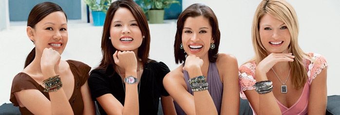 Four smiling women sitting on a sofa, each wearing stacked Cookie Lee bracelets, necklaces and earrings