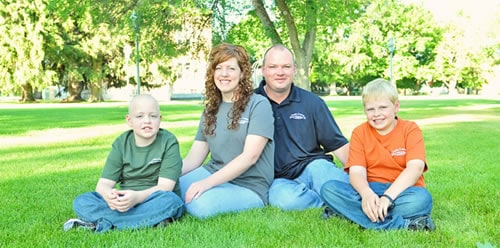 Shane and Amy Beth sitting on a lawn with their two sons, all wearing Country Gourmet Home shirts