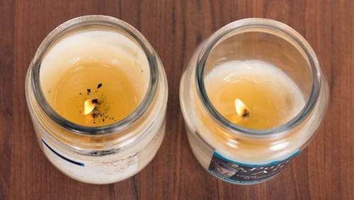 Two lit jar candles seen from above on a wooden table, one burning cleanly and one with black soot around the wick
