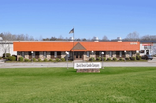 The David Oreck Candle Company factory and outlet store, a long brick building with an orange roof behind a green lawn