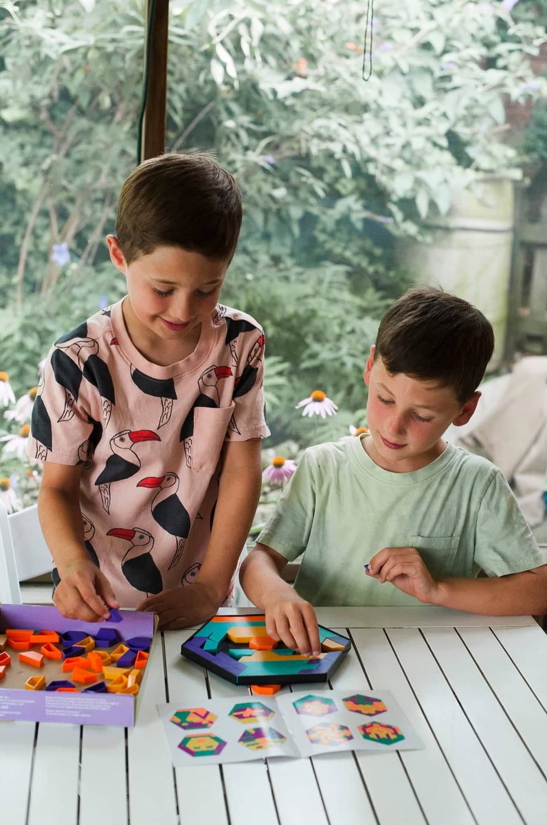 Two boys at a garden table fitting colourful Mosaic Mysteries pattern pieces into a hexagon puzzle tray