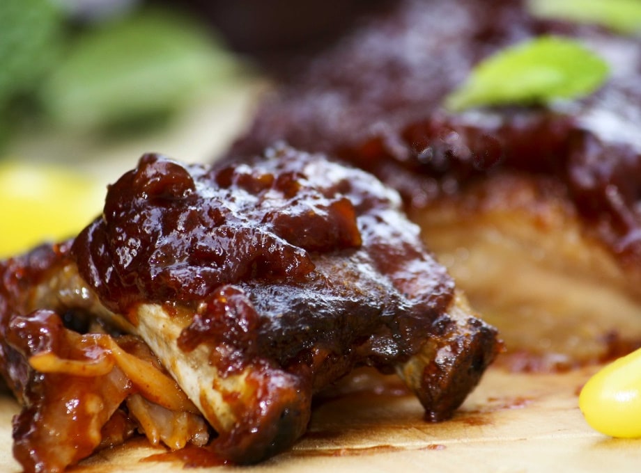 Close-up of glazed barbecue ribs on a wooden board with fresh herbs and yellow peppers