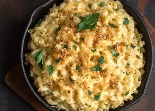 Baked macaroni and cheese with a golden crumb topping and parsley in a cast-iron skillet