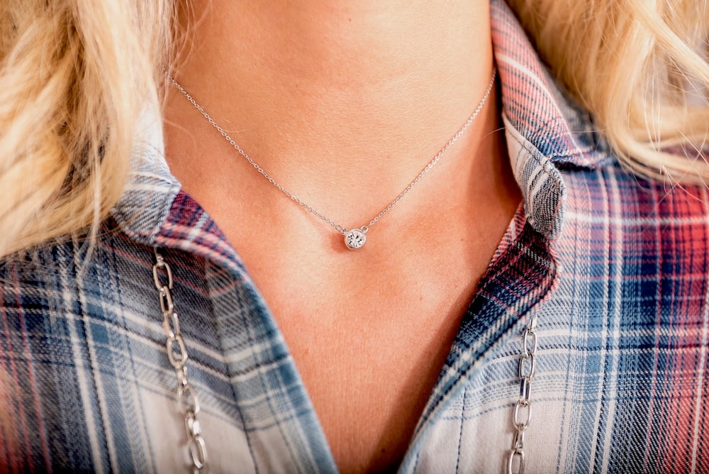 A woman in a plaid shirt wearing a fine chain necklace with a small solitaire stone