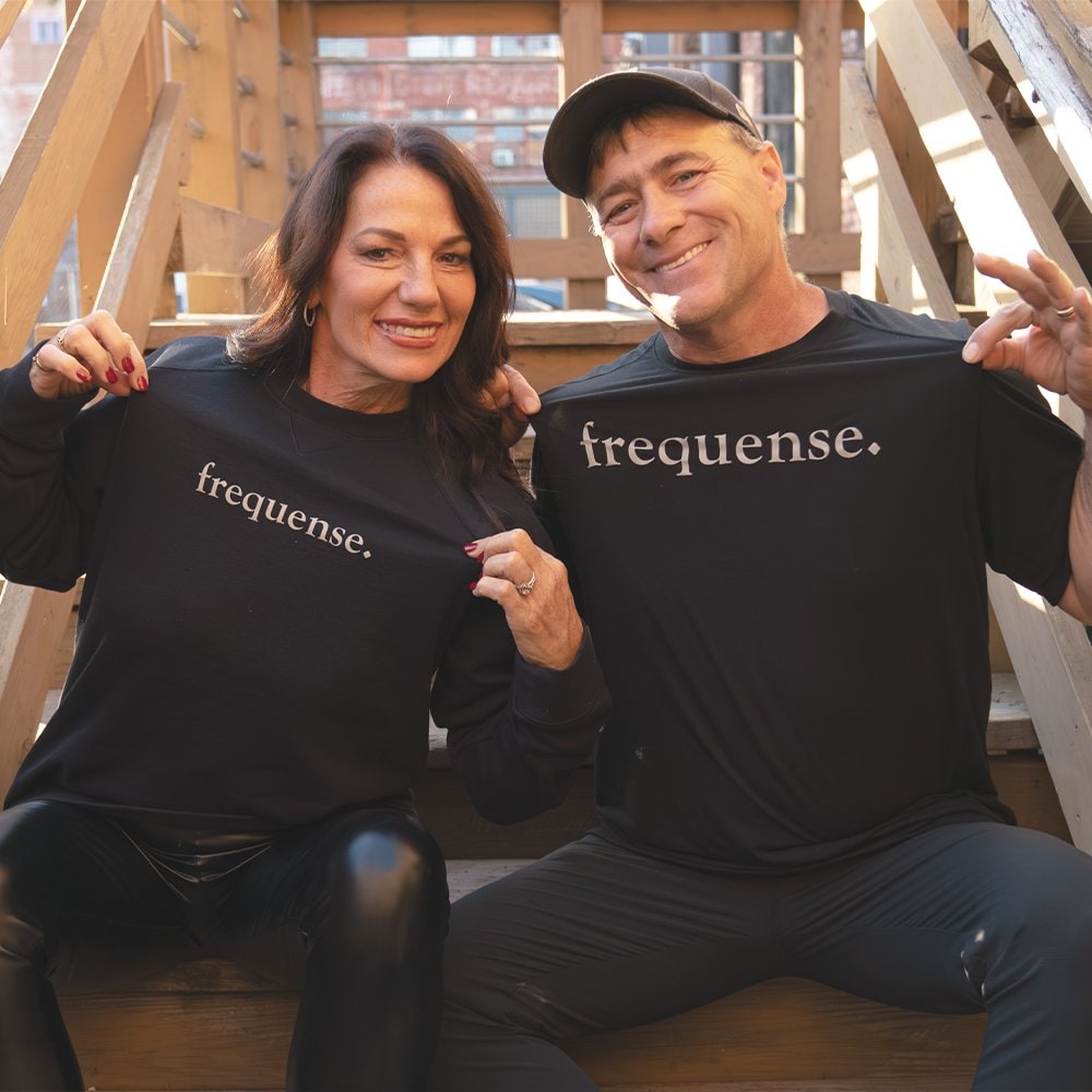 Frequense co-founders Barb and Dave Pitcock sitting on wooden steps in black Frequense shirts