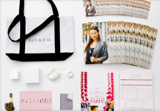 The contents of a Guy & Eva starter kit laid out on a white surface: a canvas tote, catalogs, jewelry boxes, a polishing cloth, party invitations and order forms