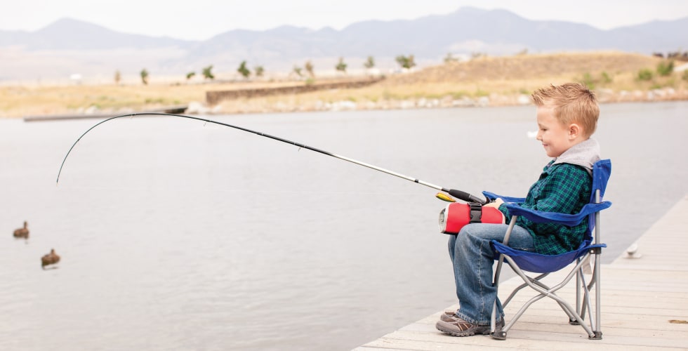 A young boy in a camping chair fishing off a dock, with a red Gherkin Pikle organizer resting on his lap