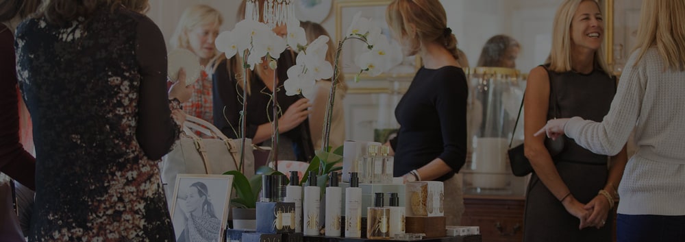 Women chatting around a display table of beauty products and white orchids at an India Hicks Get Together