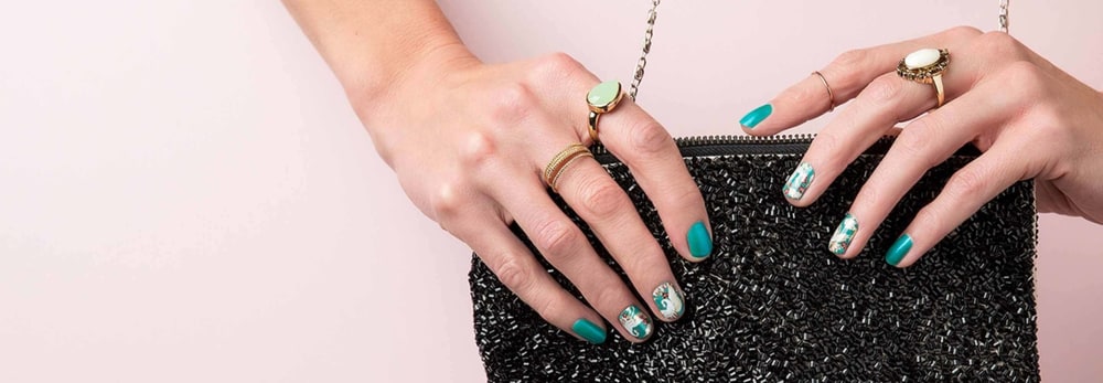 Two hands with teal Jamberry nail wraps and matching polish resting on a black beaded clutch bag