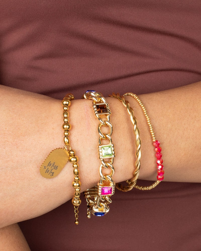Gold bracelet stack with a stamped charm and colored stones