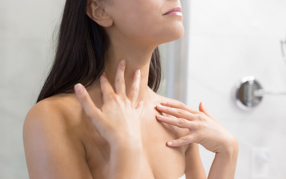 Woman applying skin care to her neck and chest in a bright bathroom