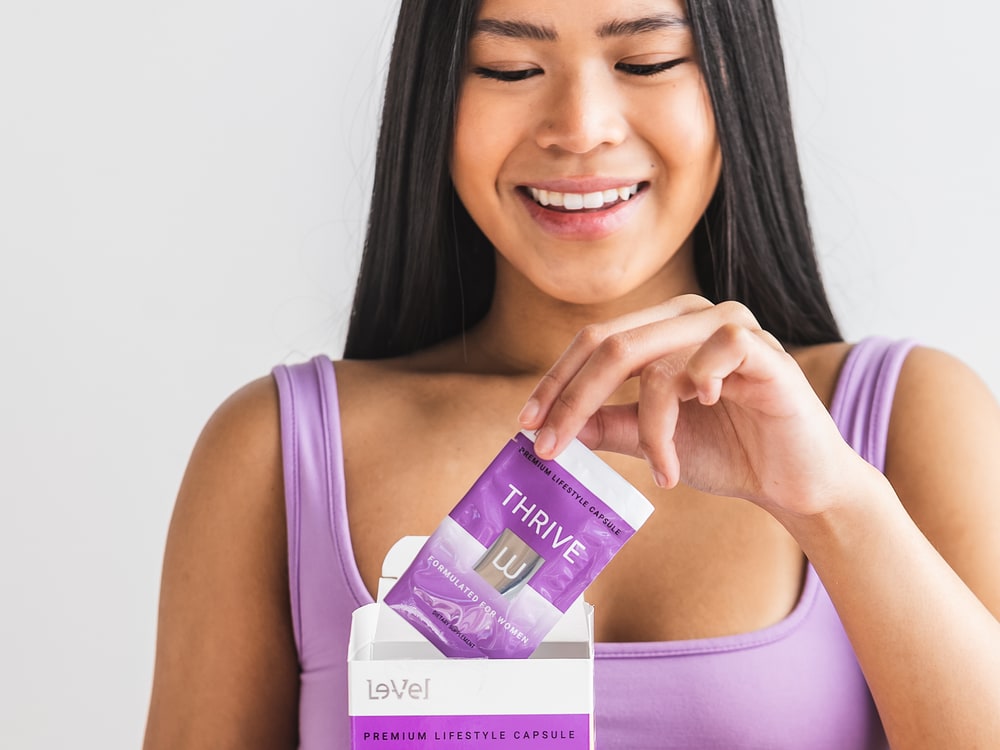 A woman smiling as she opens a THRIVE Premium Lifestyle Capsule packet