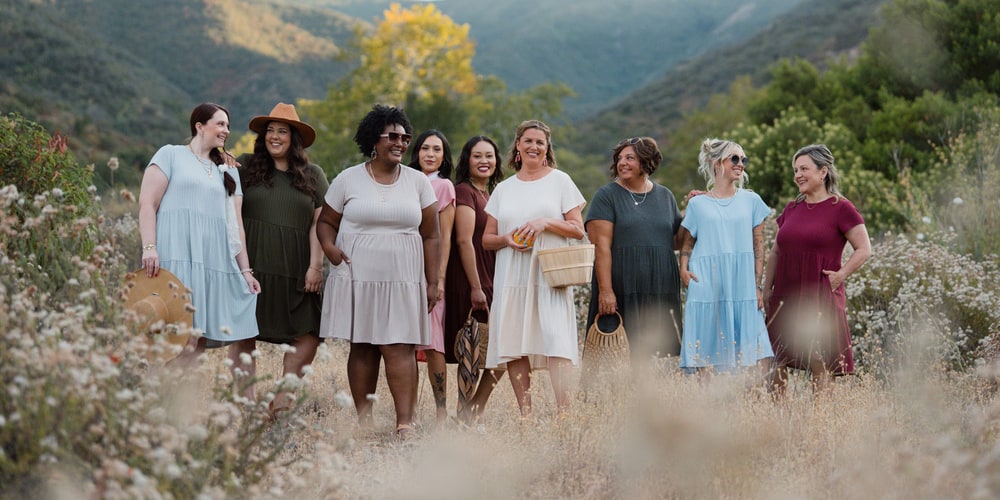 Nine women in LuLaRoe tiered dresses walking through a wildflower meadow in the hills