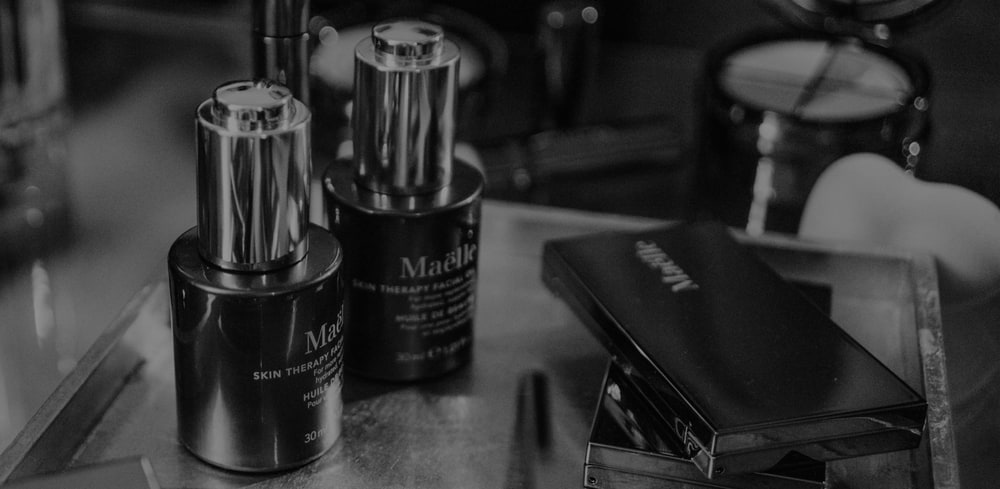 Black and white photo of two Maëlle skin care bottles and a compact on a dressing table