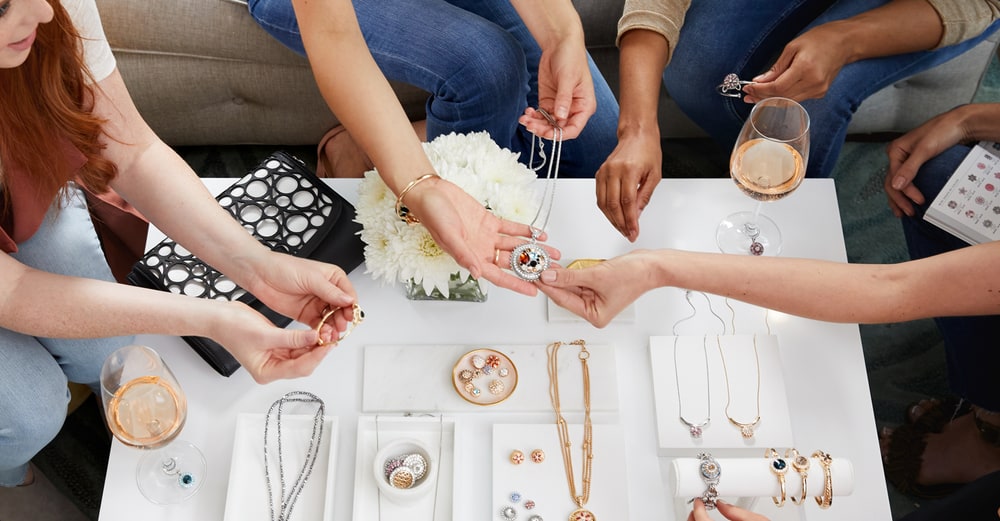 A group of women at a table trying on snap necklaces, bracelets and charms laid out on white displays