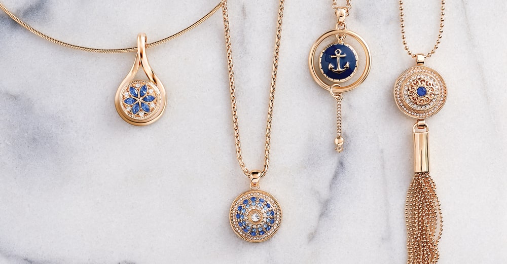 Four gold-tone snap pendants, one with a navy anchor Snap and one with a tassel, on white marble