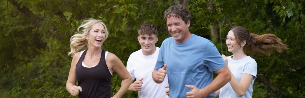 Family of four laughing as they jog together along a tree-lined path