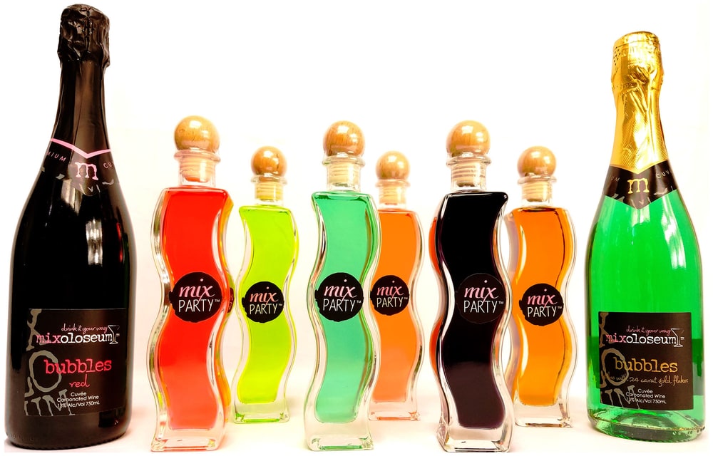 A row of brightly colored Mix Party wine cocktails in wavy glass bottles between two bottles of sparkling wine