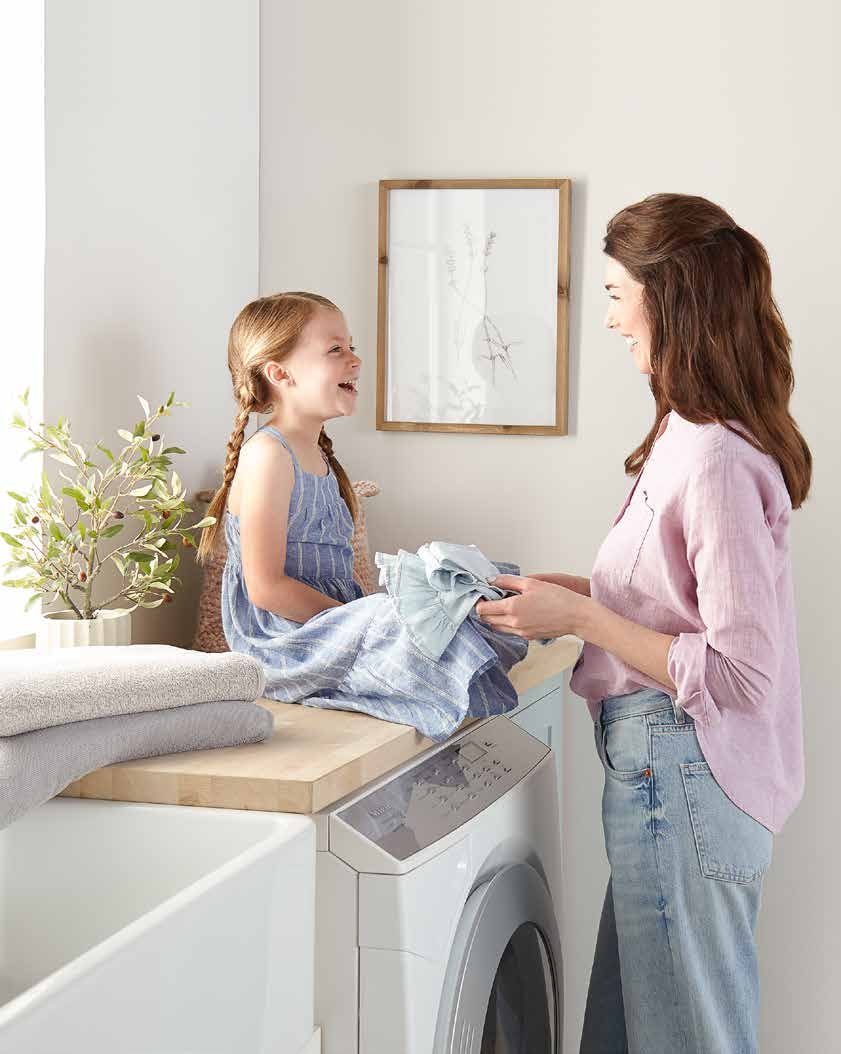 A mother and her young daughter fold laundry together on a wooden counter above a washing machine