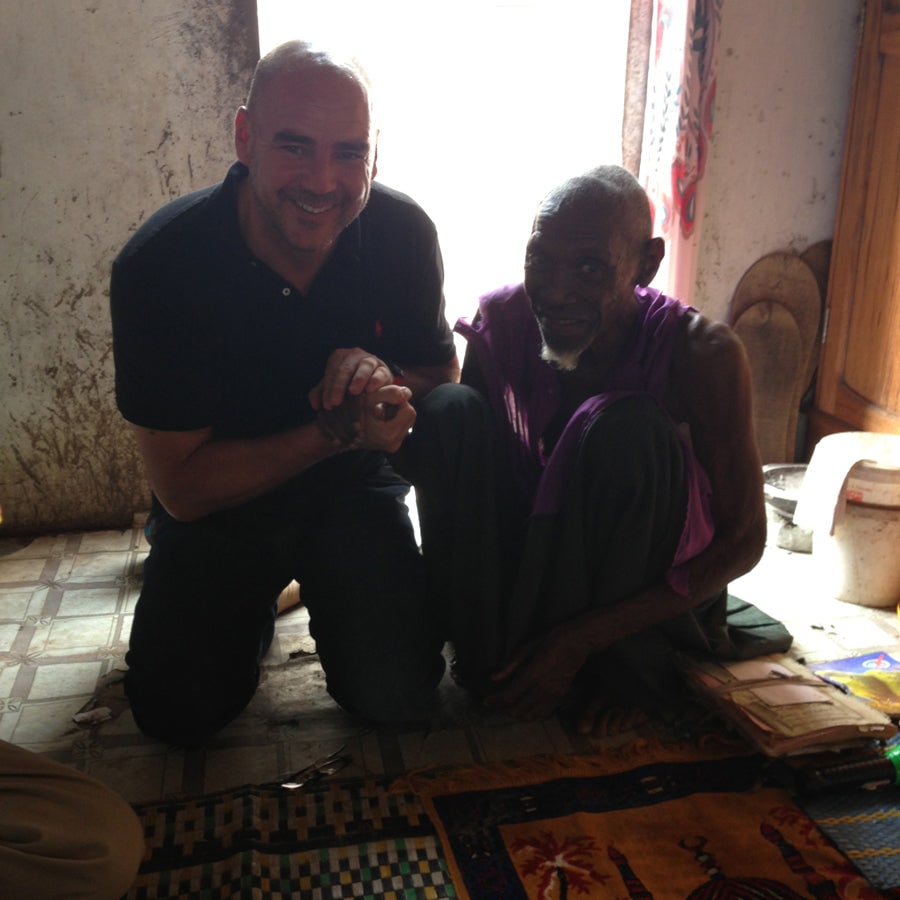 Thomas Lommel kneeling beside the village chief of Mhaba, Senegal, holding hands, in 2013