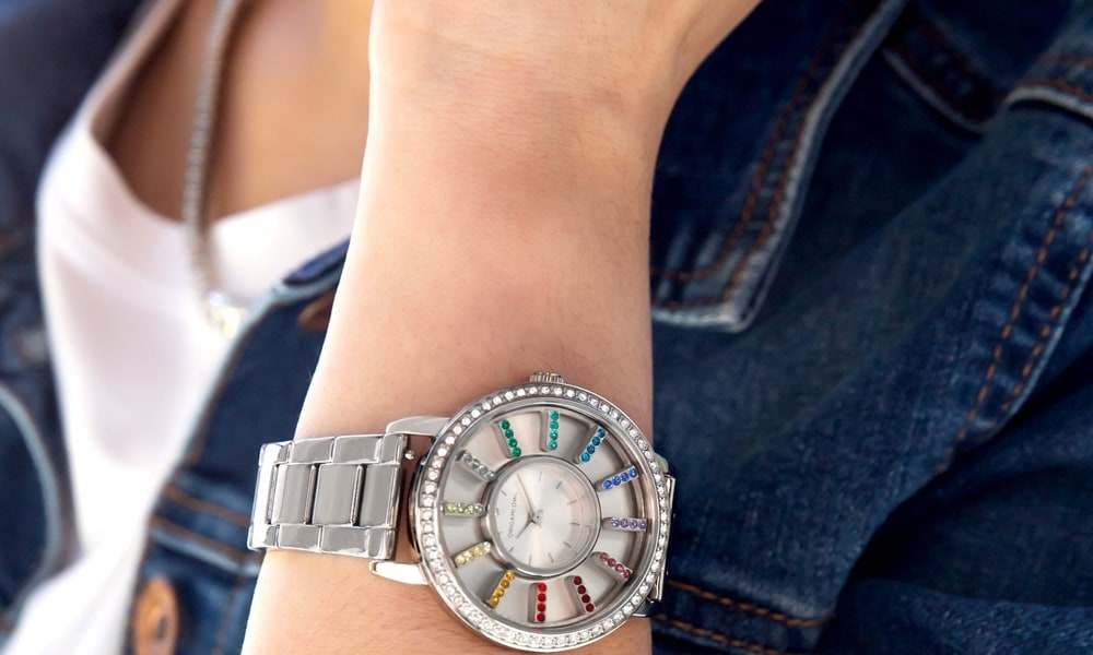 A woman in a denim jacket wearing a silver Origami Owl Living Locket watch with rainbow crystals around the dial