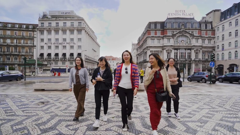 A group of women walking across a patterned square in Lisbon, smiling