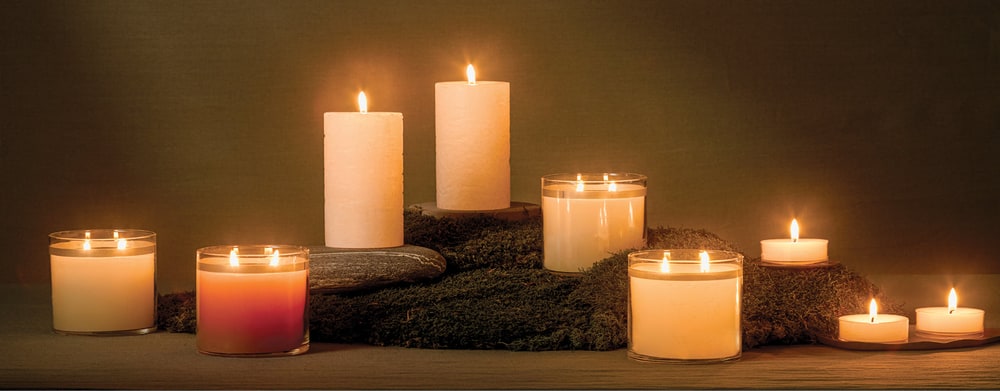 Lit PartyLite pillar candles, jar candles and tealights arranged on moss and stone in a dim room