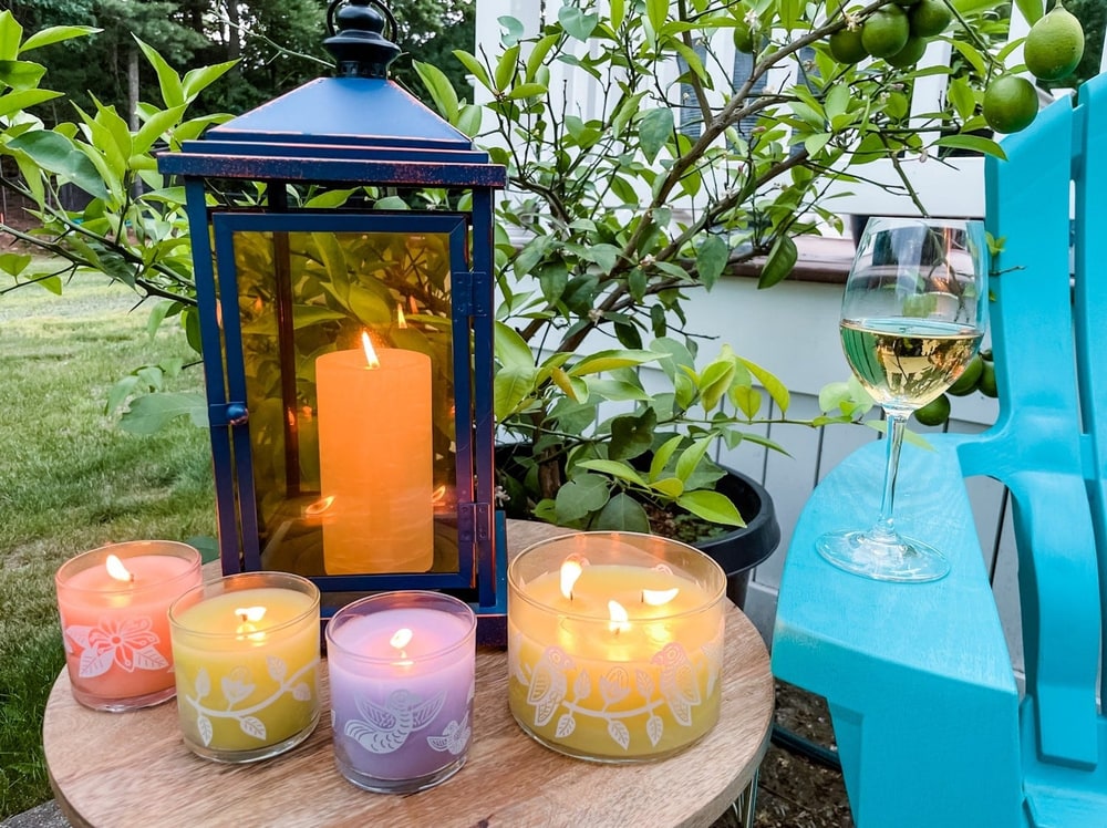 PartyLite citronella jar candles and a pillar candle in a blue lantern on a garden table at dusk