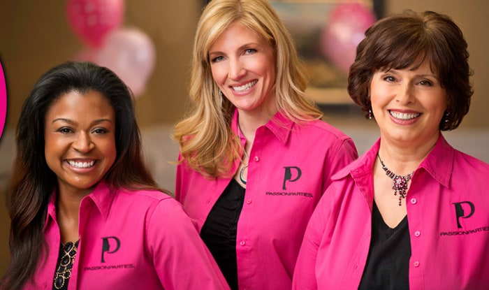 Three Passion Parties Consultants in matching pink company shirts smiling in front of party balloons
