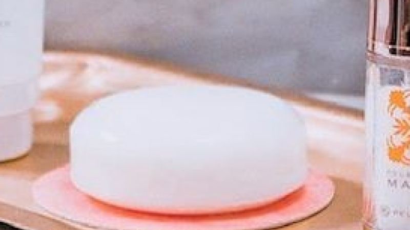 A round white Aolani facial soap on a pink dish beside a Mahina serum bottle on a bathroom counter
