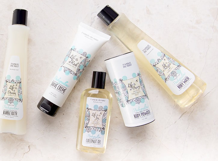 Perfectly Posh bubble bath, shave crème, coconut oil, body powder and body wash bottles laid out on a pale marble surface