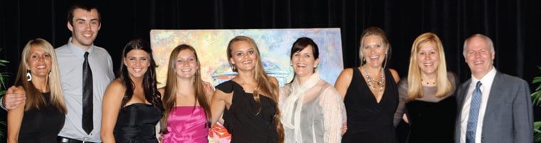 A row of Pink Papaya leaders and team members in evening dress posing in front of a painting at a company event