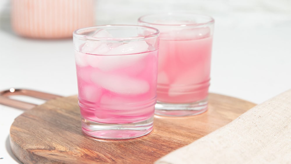 Two glasses of pink iced Plexus Slim drink on a round wooden board