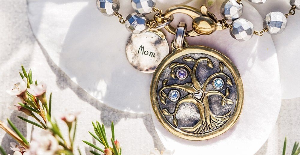 A tree of life pendant set with three birthstones beside a small Mom charm on a beaded chain