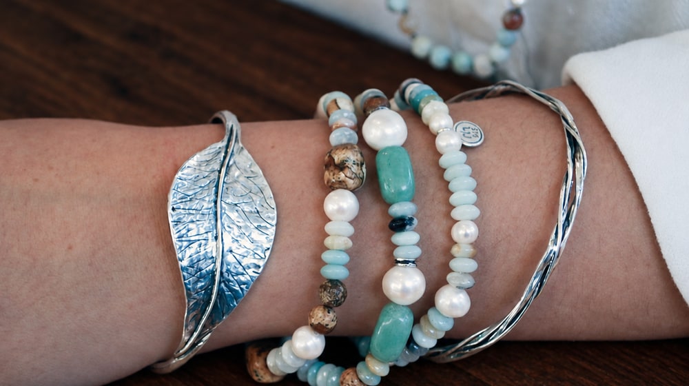 A wrist stacked with a silver leaf cuff, beaded amazonite and pearl stretch bracelets and a twisted silver bangle