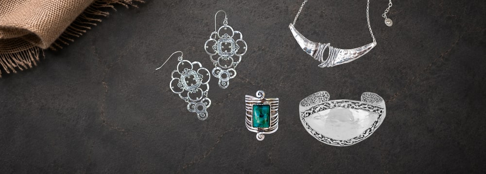 Silver filigree earrings, a turquoise-set ring, a cuff and a crescent necklace laid out on dark slate