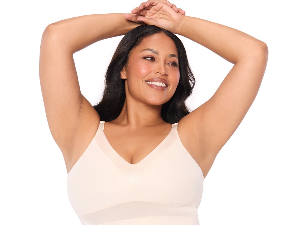 A smiling woman with her arms raised, wearing a cream Ruby Ribbon shaping cami