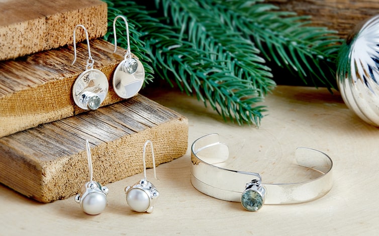 Sterling silver drop earrings with blue stones and pearls beside a silver cuff bracelet on a wooden table